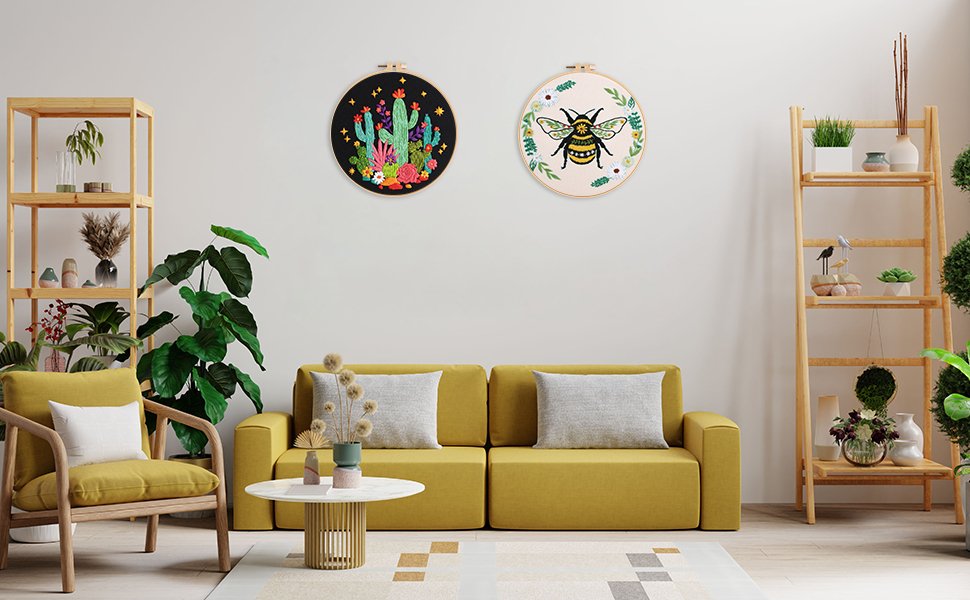 Two embroidered hoops, one with cacti and flowers, the other with a bee, hanging on a wall above a yellow sofa.