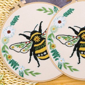 Two embroidery hoops with bee and floral designs, one slightly behind the other.