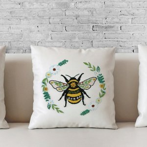 Embroidery kit design of a bee surrounded by flowers and leaves on a white pillow.