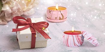 Two lit candles in decorative tins next to a gift box with a red ribbon.