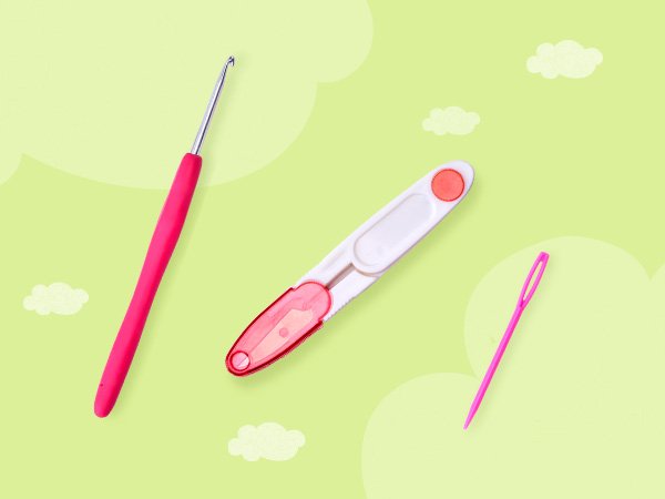 Crochet hook, scissors, and needle laid out on a light green background with white cloud shapes.