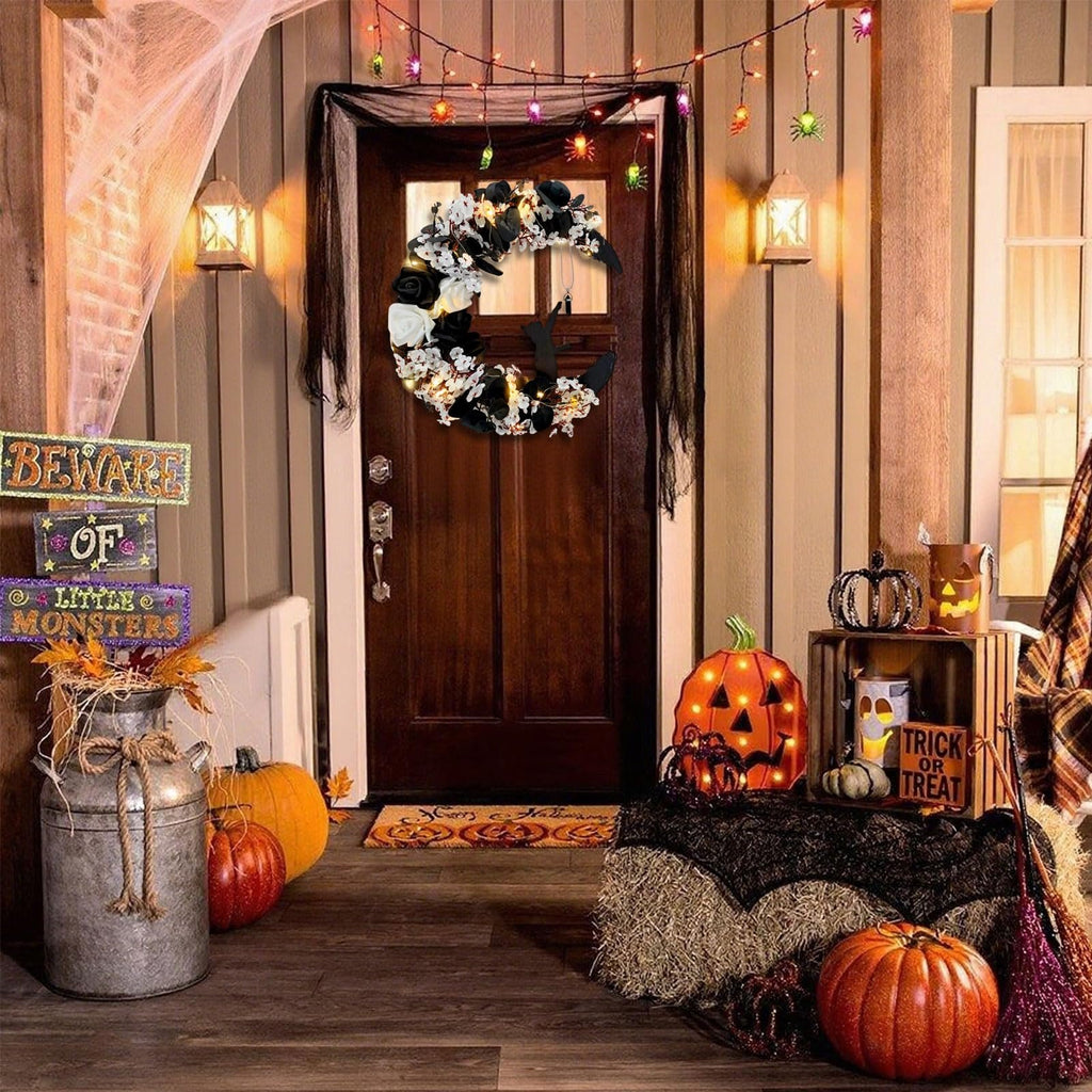 Halloween porch decor with a crescent moon wreath on the door, pumpkins, and spooky lights