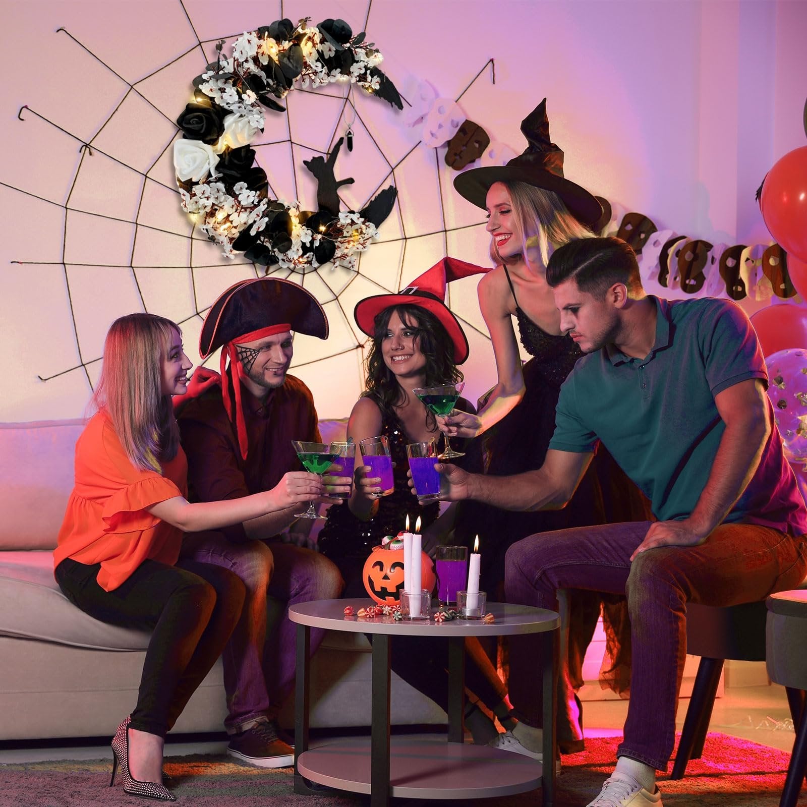 Group of friends in Halloween costumes toasting drinks around a table with a crescent moon wreath