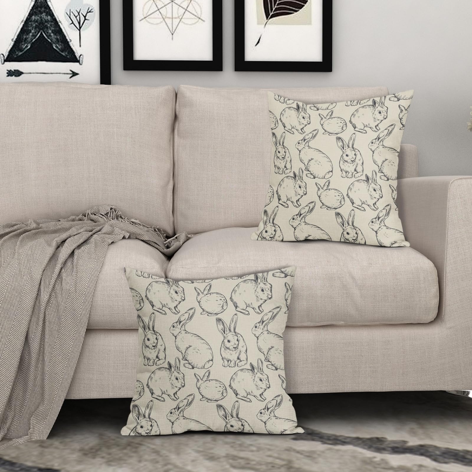 Two linen throw pillow covers with a black bunny sketch pattern displayed on a sofa.