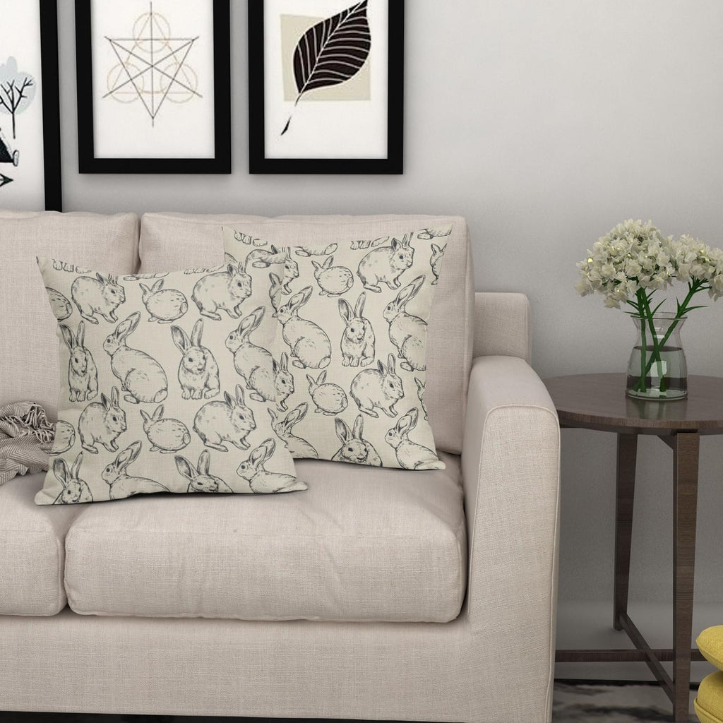 Two linen throw pillow covers with a black Easter bunny sketch pattern on a sofa.