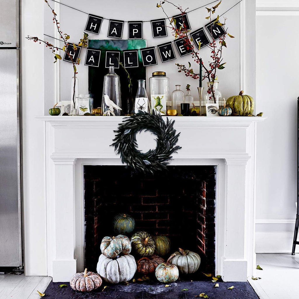 Black feather wreath hanging on a fireplace mantel with Halloween decorations and pumpkins below