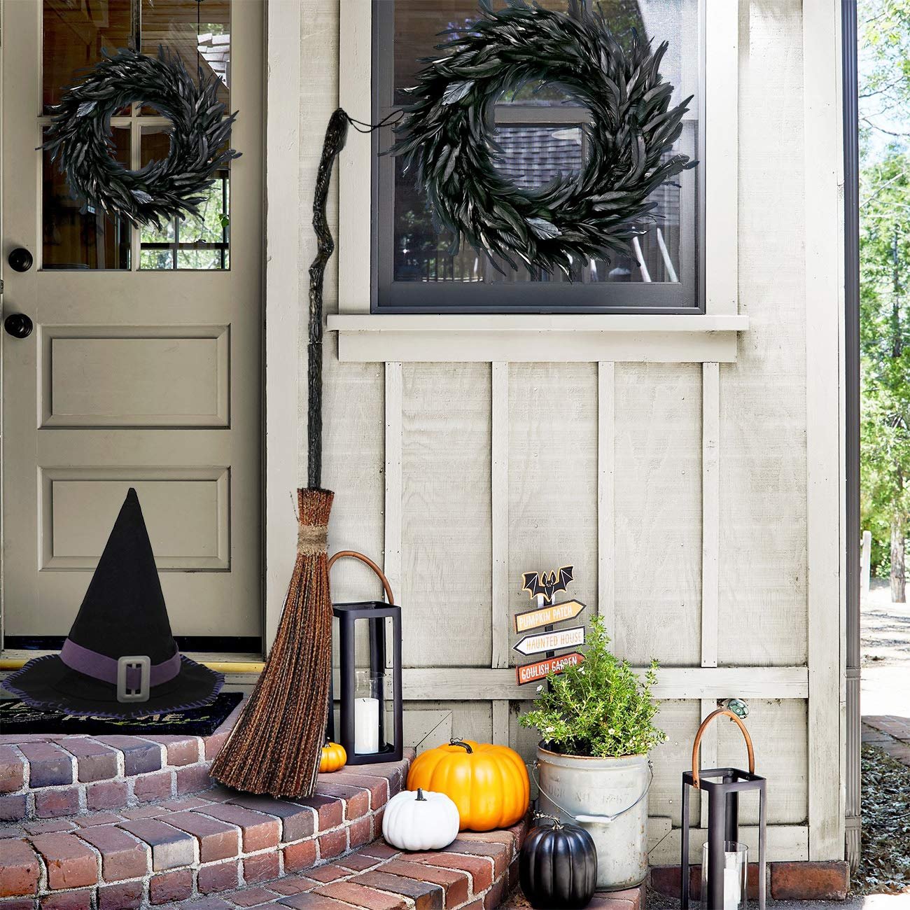 Black feather wreaths and Halloween decorations on a porch, including a witch hat, broom, pumpkins, and lanterns.
