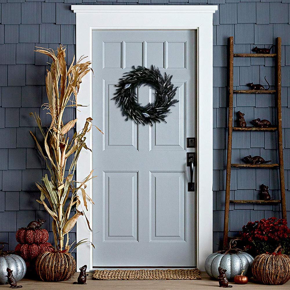 Black feather wreath hanging on a light blue door with Halloween decorations including pumpkins and a ladder with mice