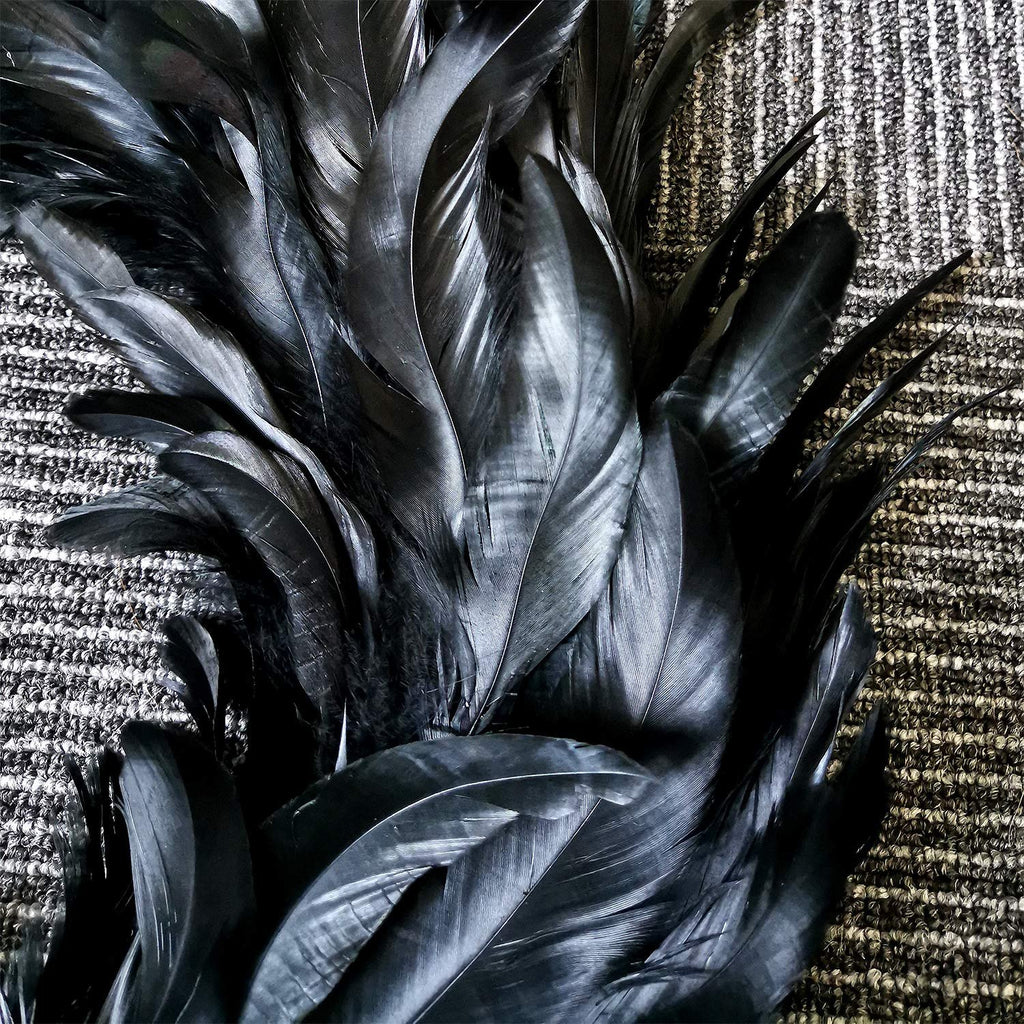 Close-up of a black feather wreath on a textured background, showing the detail and arrangement of the feathers.