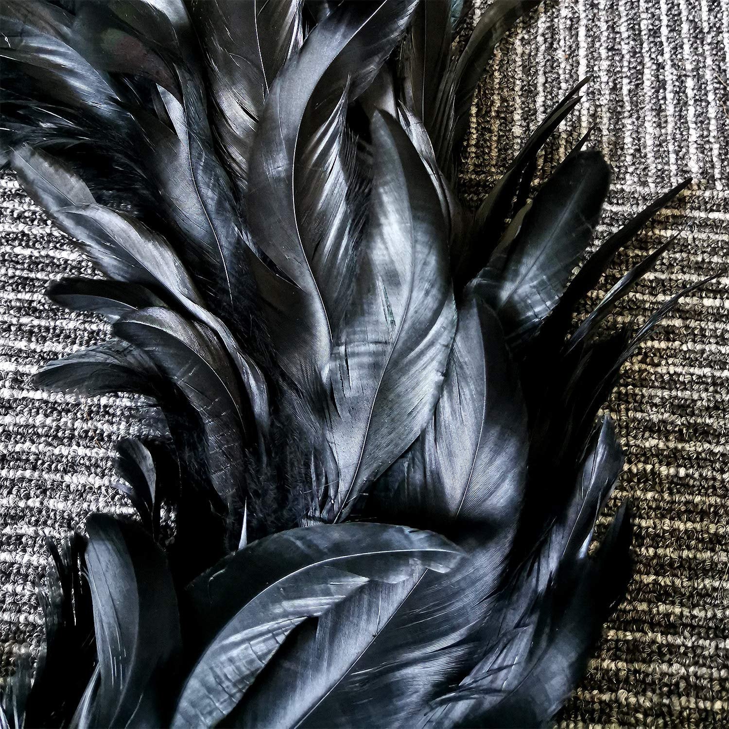 Close-up of a black feather wreath on a textured background, showing the detail and arrangement of the feathers.