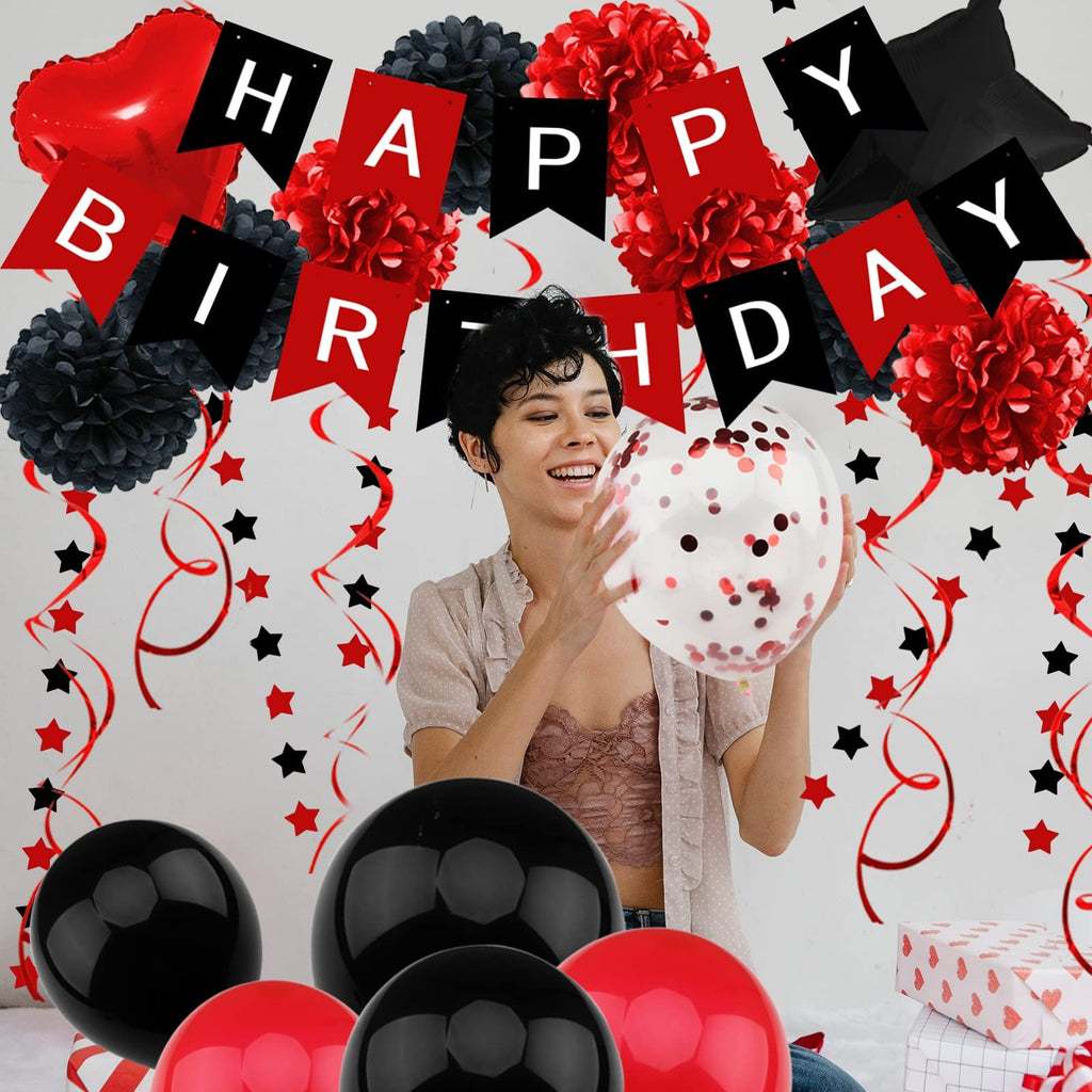 Woman holding a confetti balloon at a black and red birthday party with banner, pompoms, and balloons