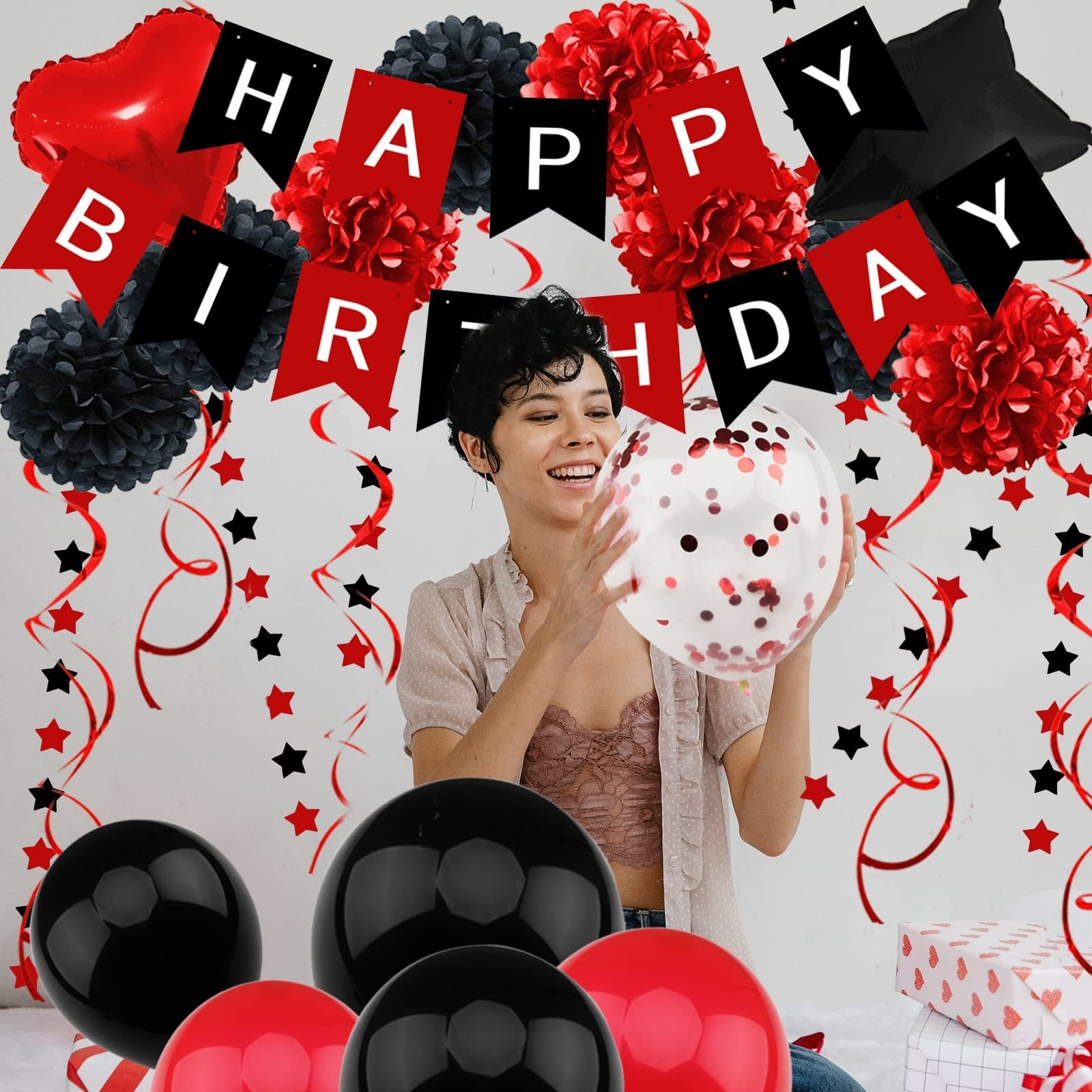 Woman holding a confetti balloon at a black and red birthday party with banner, pompoms, and balloons