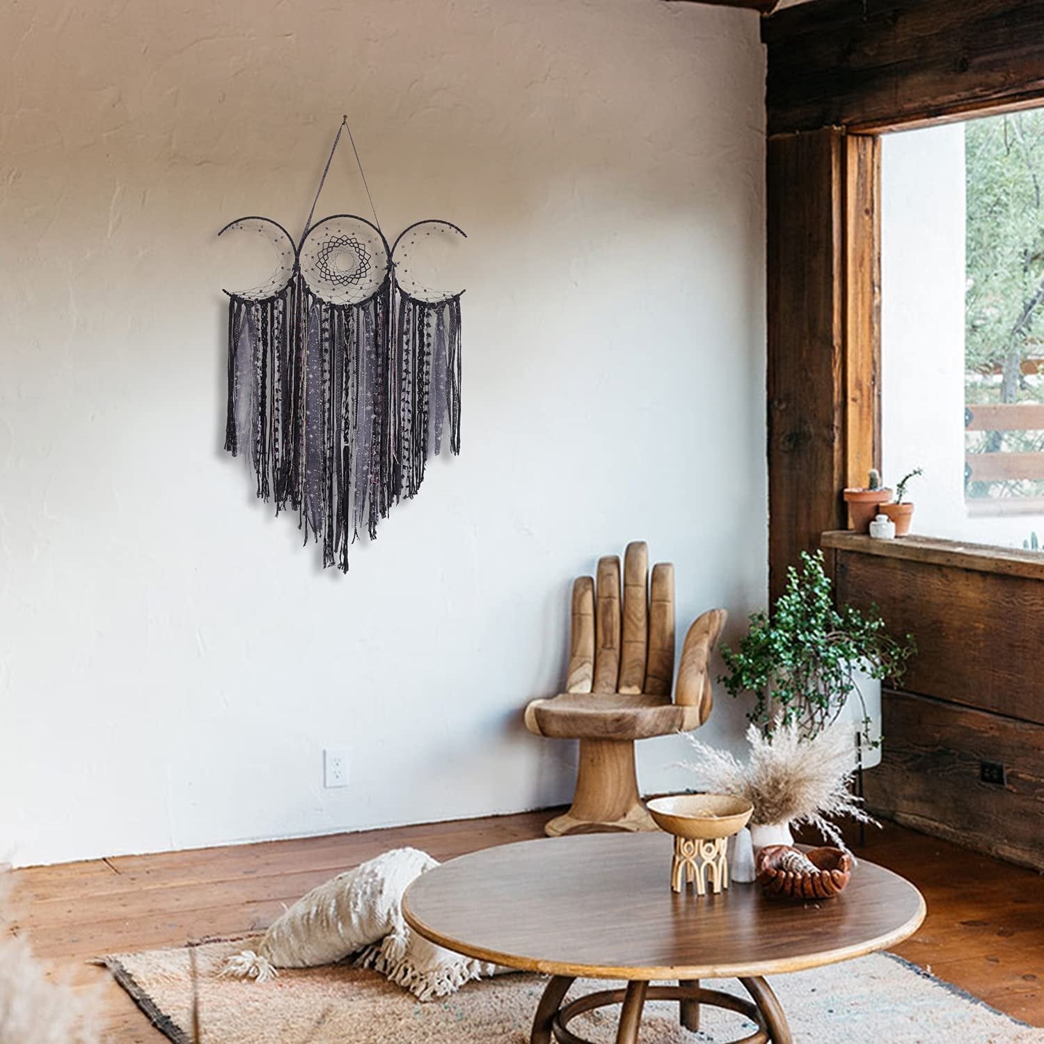 Black triple moon macrame wall hanging with crescent dream catchers and textile fringe, displayed on a white wall in a bohemian-style room.