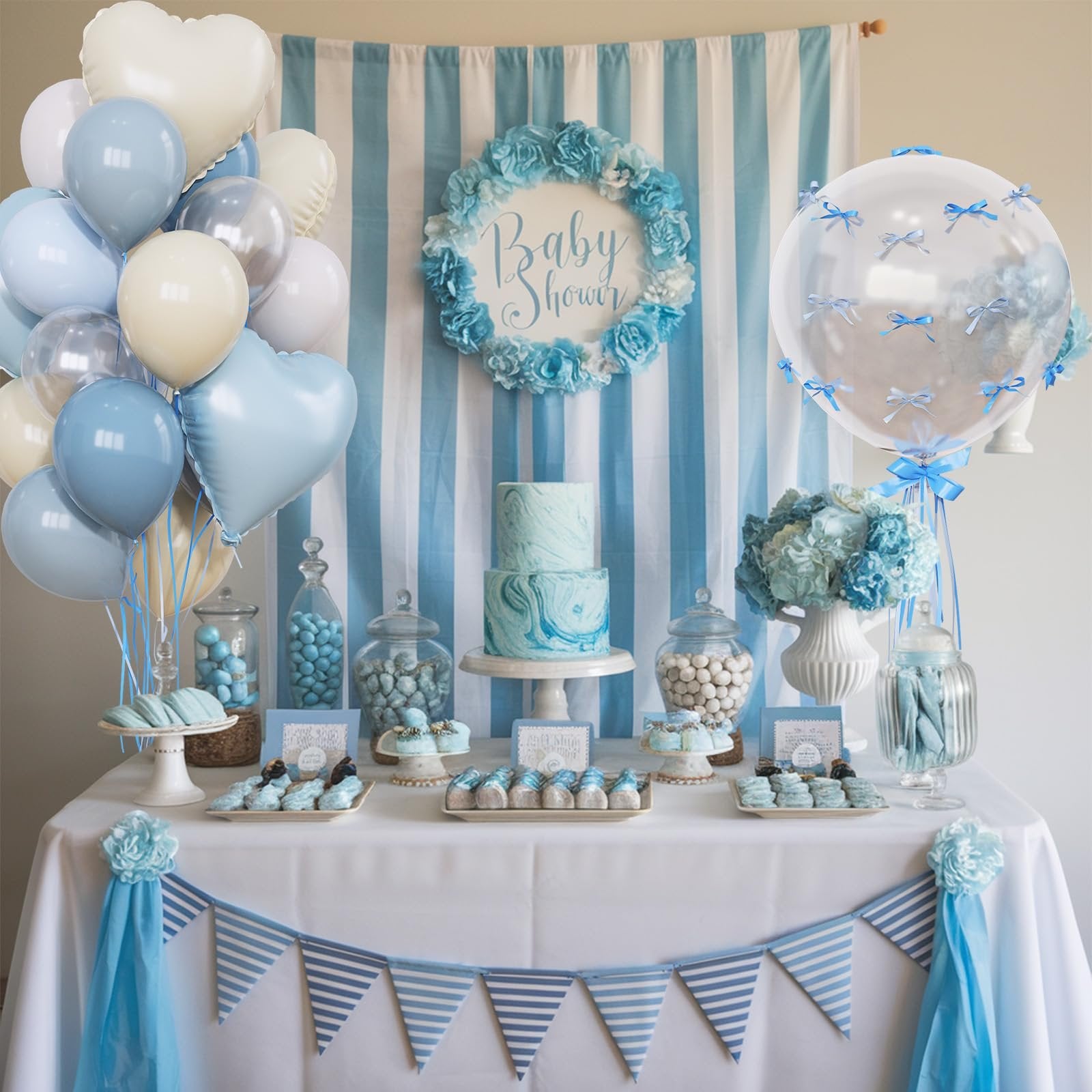 Baby shower dessert table with blue and white striped backdrop, cake, macarons, candy jars, and balloons.