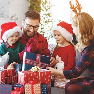 Family opening Christmas gifts, wearing Santa hats and antlers, with a decorated Christmas tree in the background.