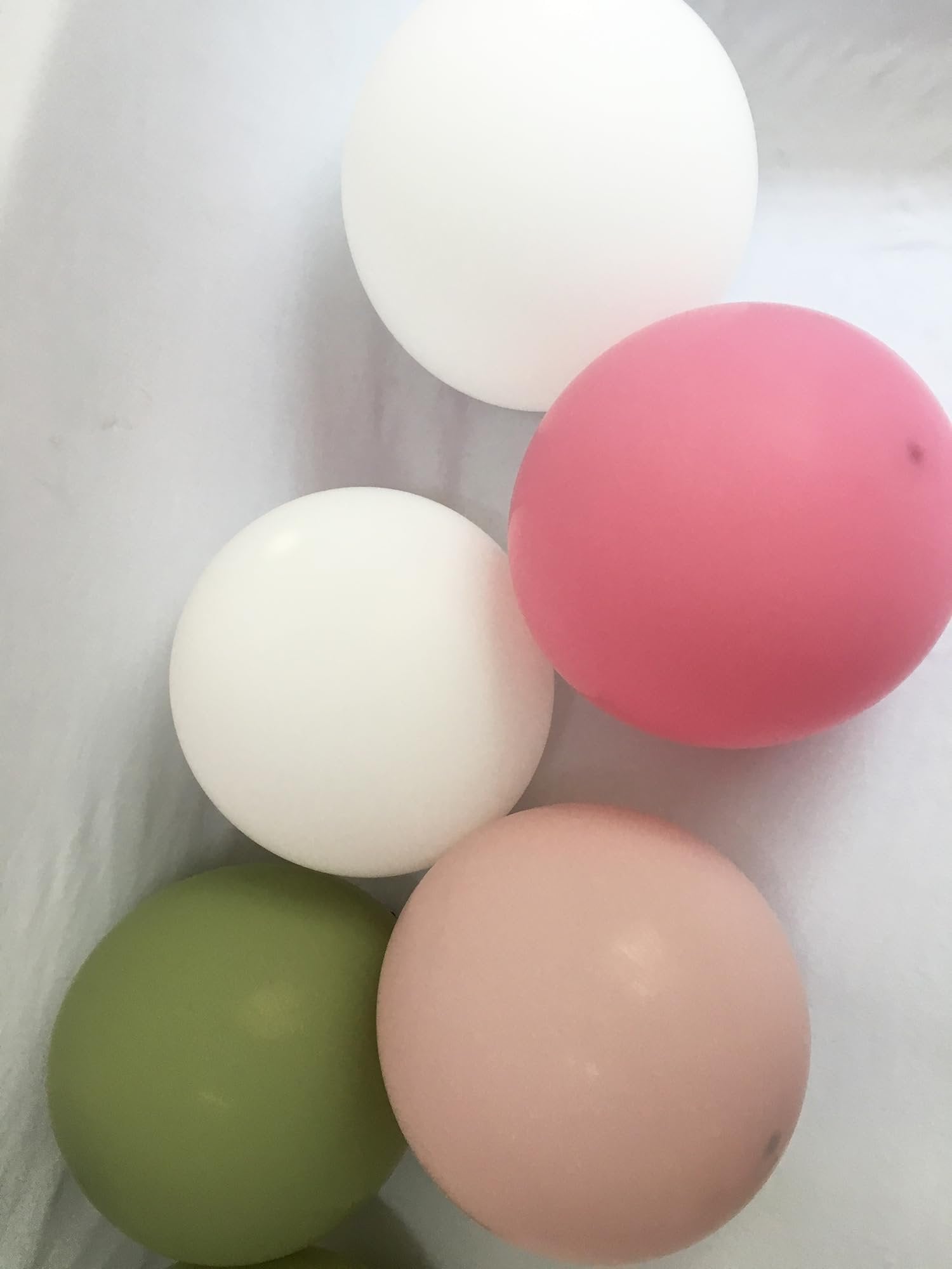 Five round balloons in white, pink, sage green, and rose pink arranged on a white textured surface.