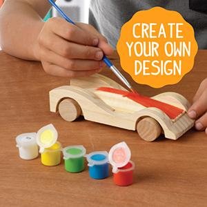 Child painting a wooden race car kit with small pots of acrylic paint