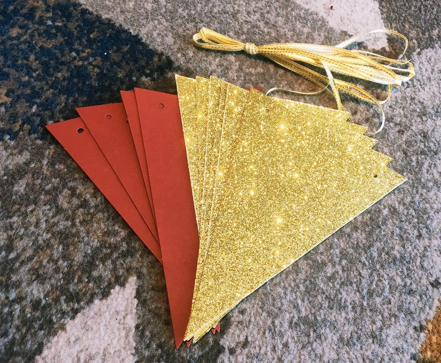 Burgundy and gold glitter triangle bunting garland pieces with gold ribbon on a textured surface