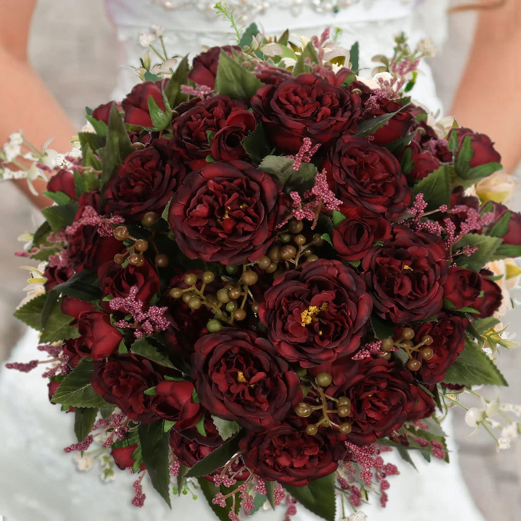 Burgundy artificial peony bouquet held by a person in a white dress, featuring multiple flower heads and greenery.
