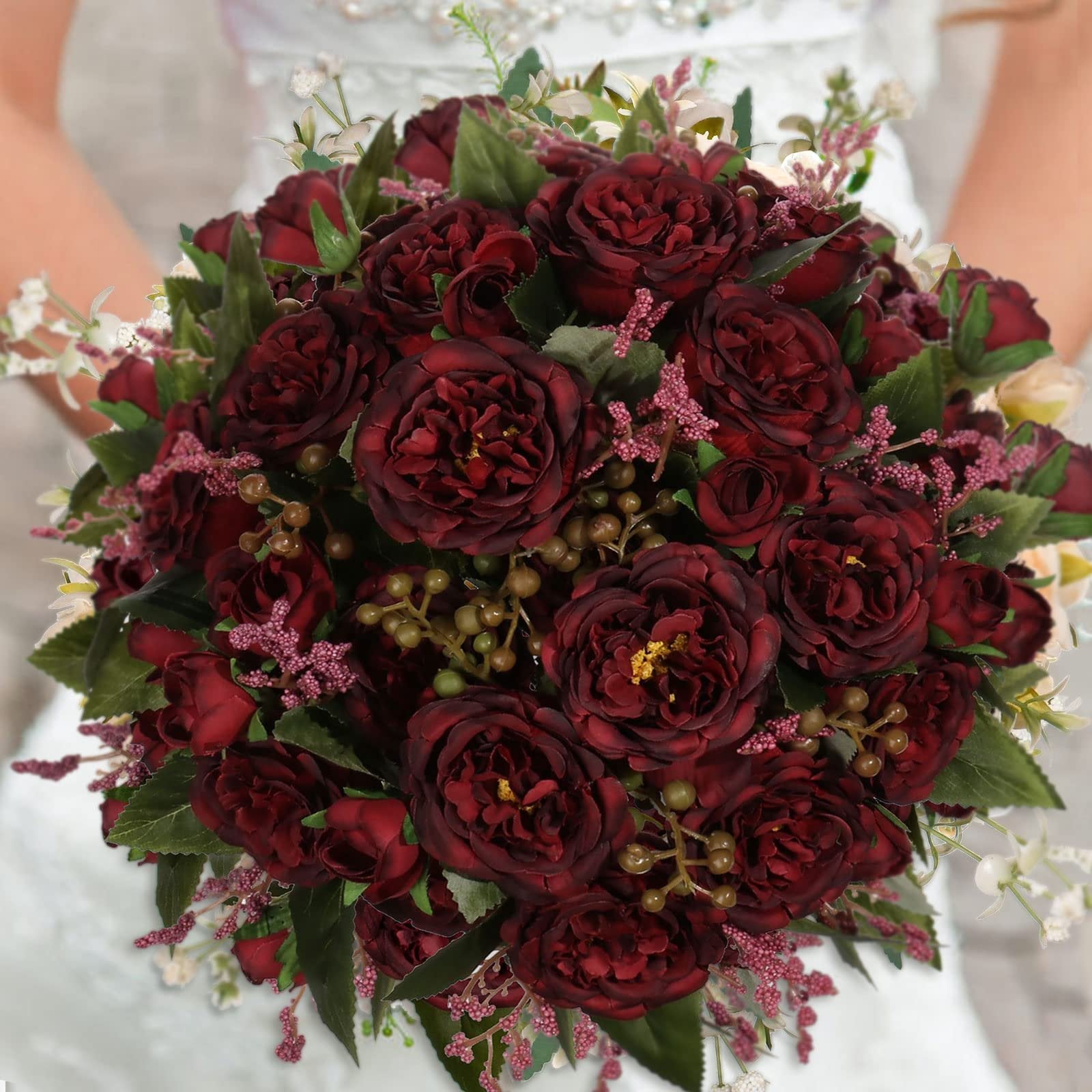 Burgundy artificial peony bouquet held by a person in a white dress, featuring multiple flower heads and greenery.