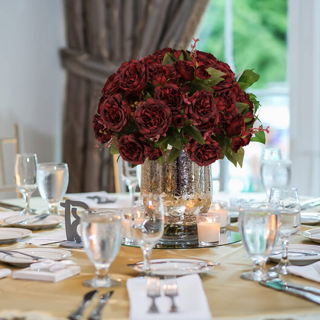 Burgundy artificial peony bouquet centerpiece on a decorated table with place settings and candles.