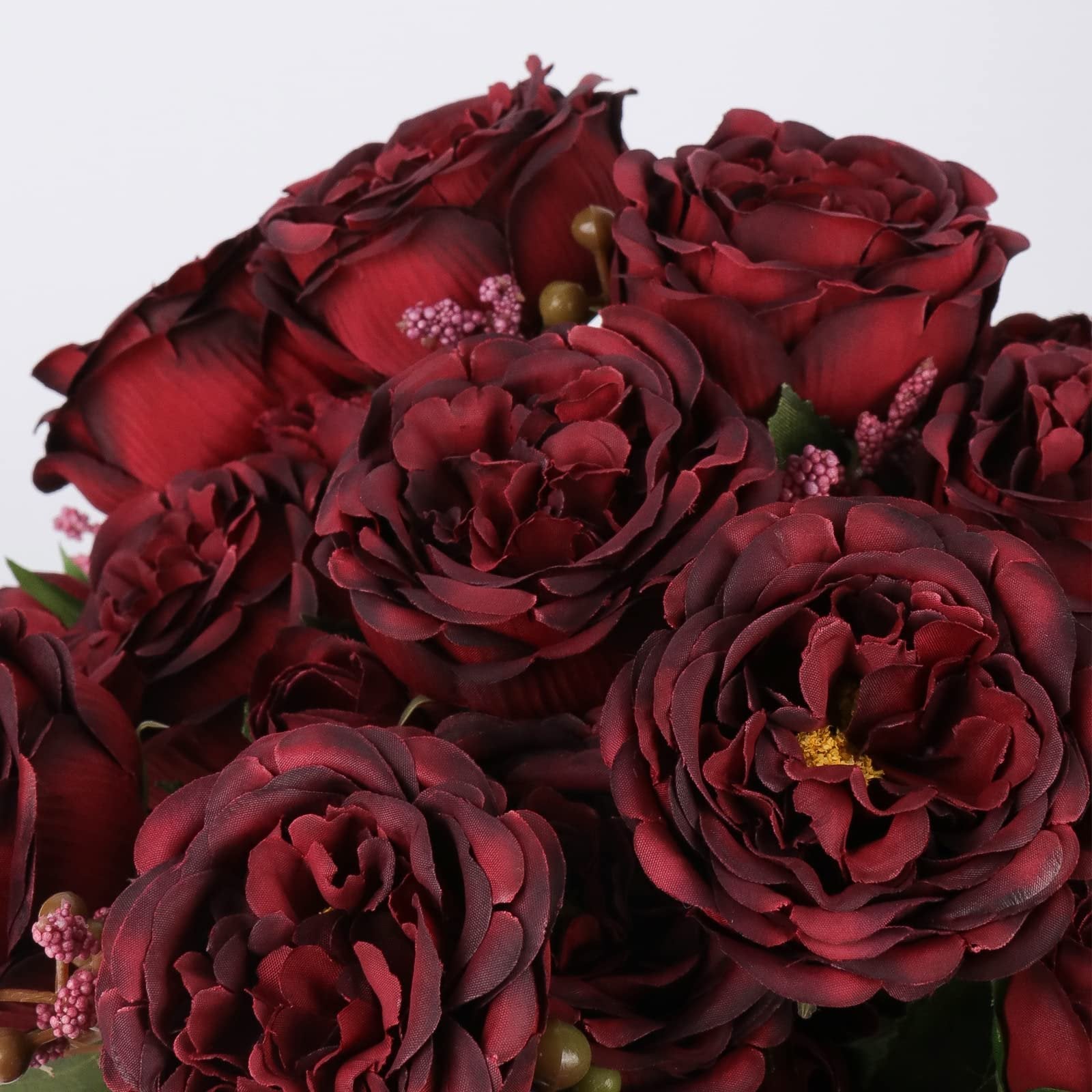 Close-up of burgundy artificial peonies with multiple flower heads and small pink buds against a white background.