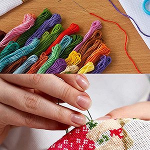 Close-up of hands cross-stitching with colorful threads and needles, showing a partially completed pattern.