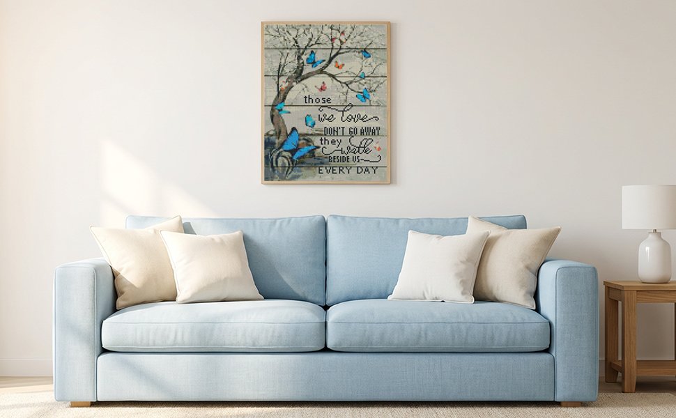 Framed butterfly tree cross-stitch art hanging above a light blue sofa with cream pillows.