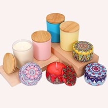 Collection of various candle containers including glass jars, colored tins, and wooden lids, arranged on wooden blocks.