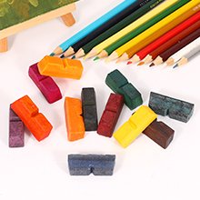 Assorted colored wax blocks and colored pencils arranged on a white surface with a small easel in the background.