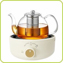 Glass teapot with infuser filled with amber liquid, sitting on a cream-colored electric hot plate with a control dial.