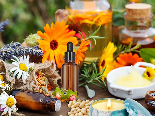 Candle making ingredients including soy wax, essential oils, dried flowers, and a lit candle in a tin.