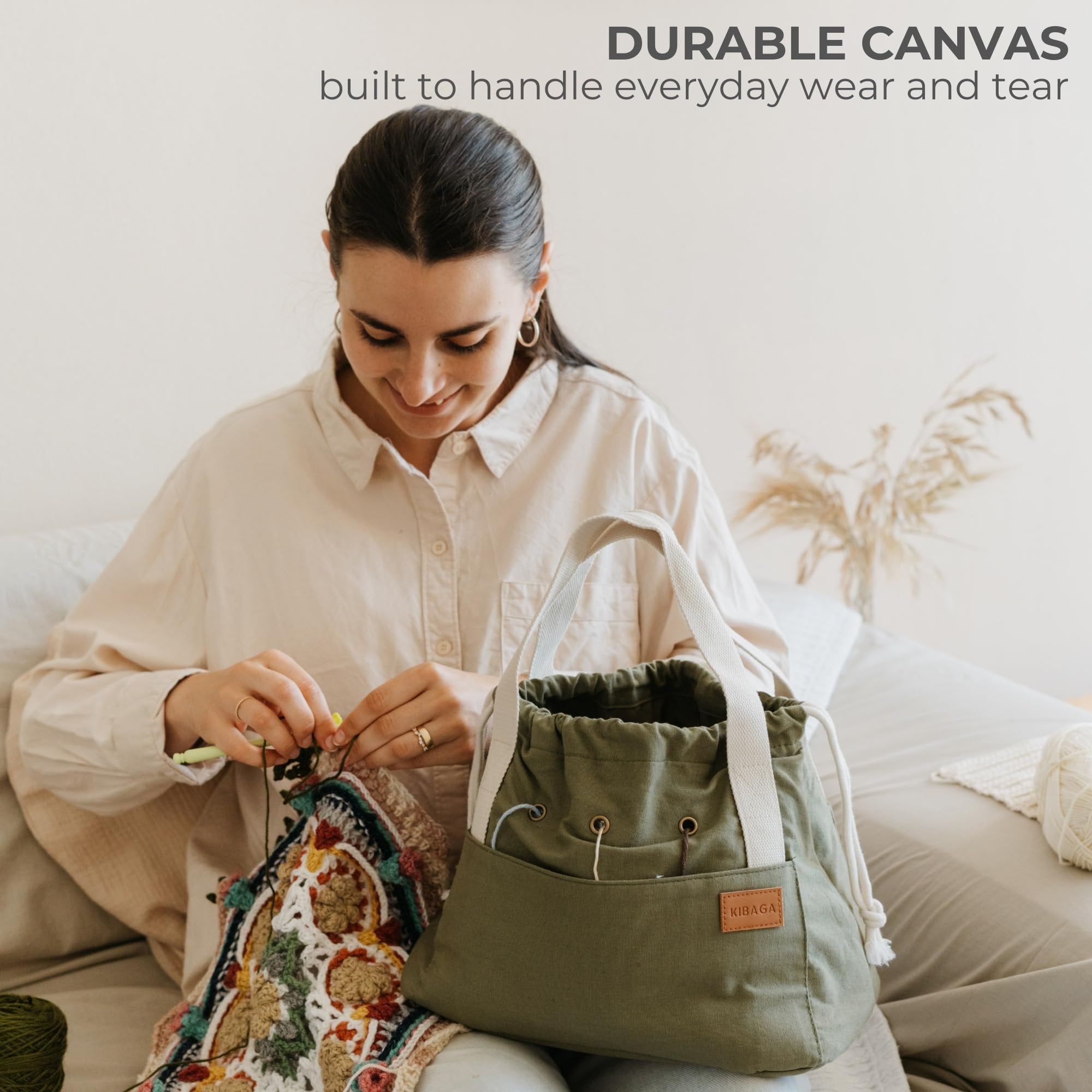 Woman crocheting with a green canvas bag organizer next to her, showing pockets and handles.