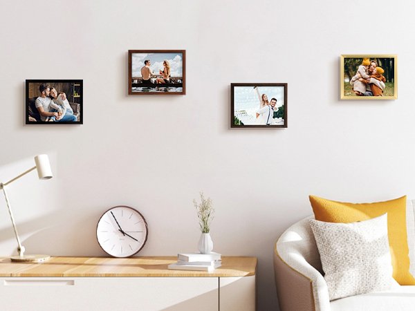 Four framed photos displayed on a wall above a desk with a lamp and clock.