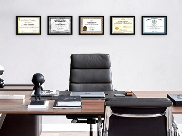 Five framed certificates displayed on a wall above a desk with a leather office chair.