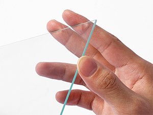 Close-up of a hand holding a thin sheet of clear glass with a slight blue tint.