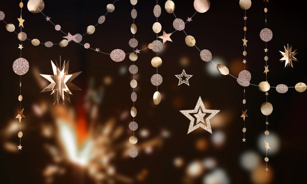 Champagne gold star and circle garlands with glitter accents hanging against a dark, bokeh background.