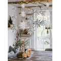 Hanging 3D paper snowflake ornaments in white and silver decorate a room with a table setting and window.