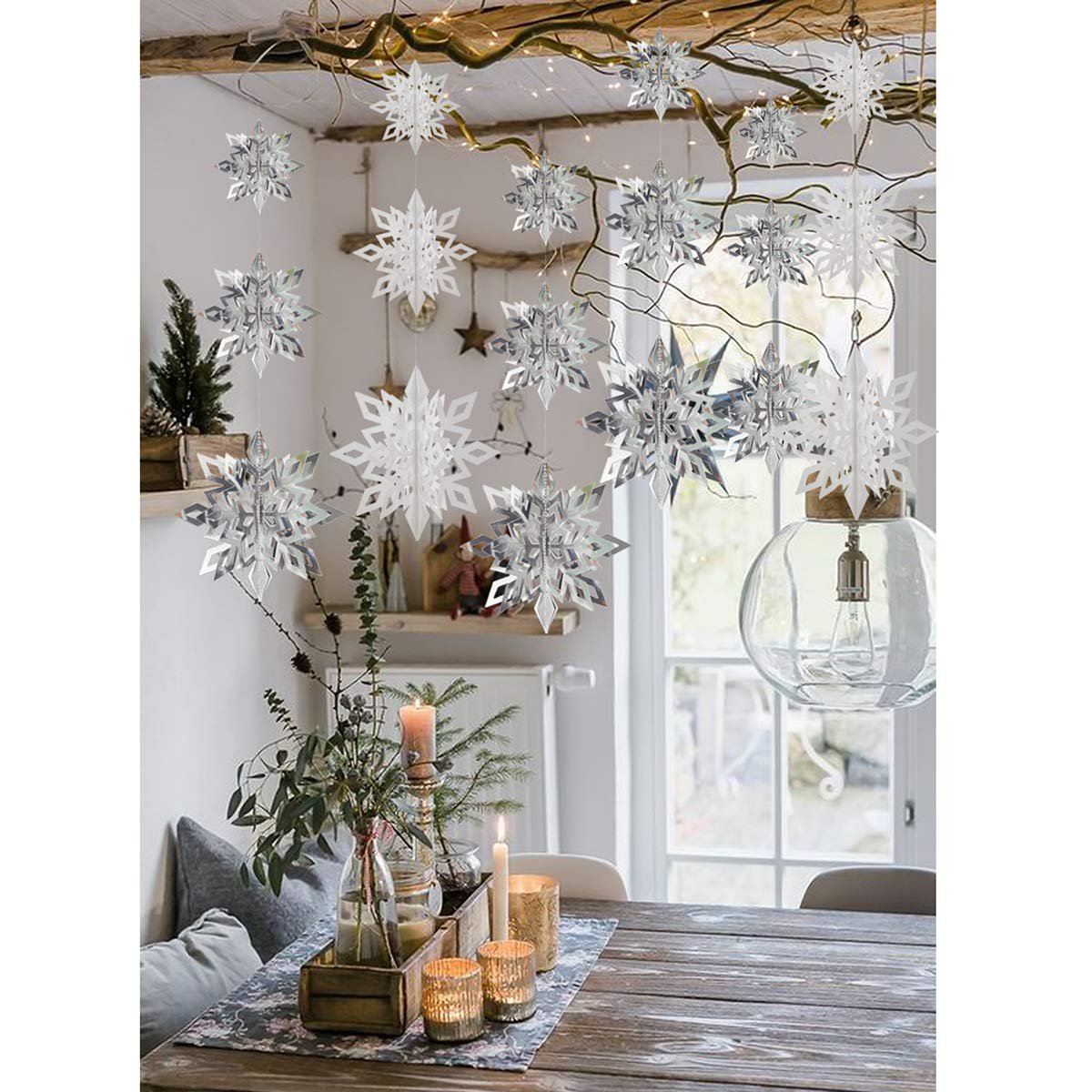 Hanging 3D paper snowflake ornaments in white and silver decorate a room with a table setting and window.