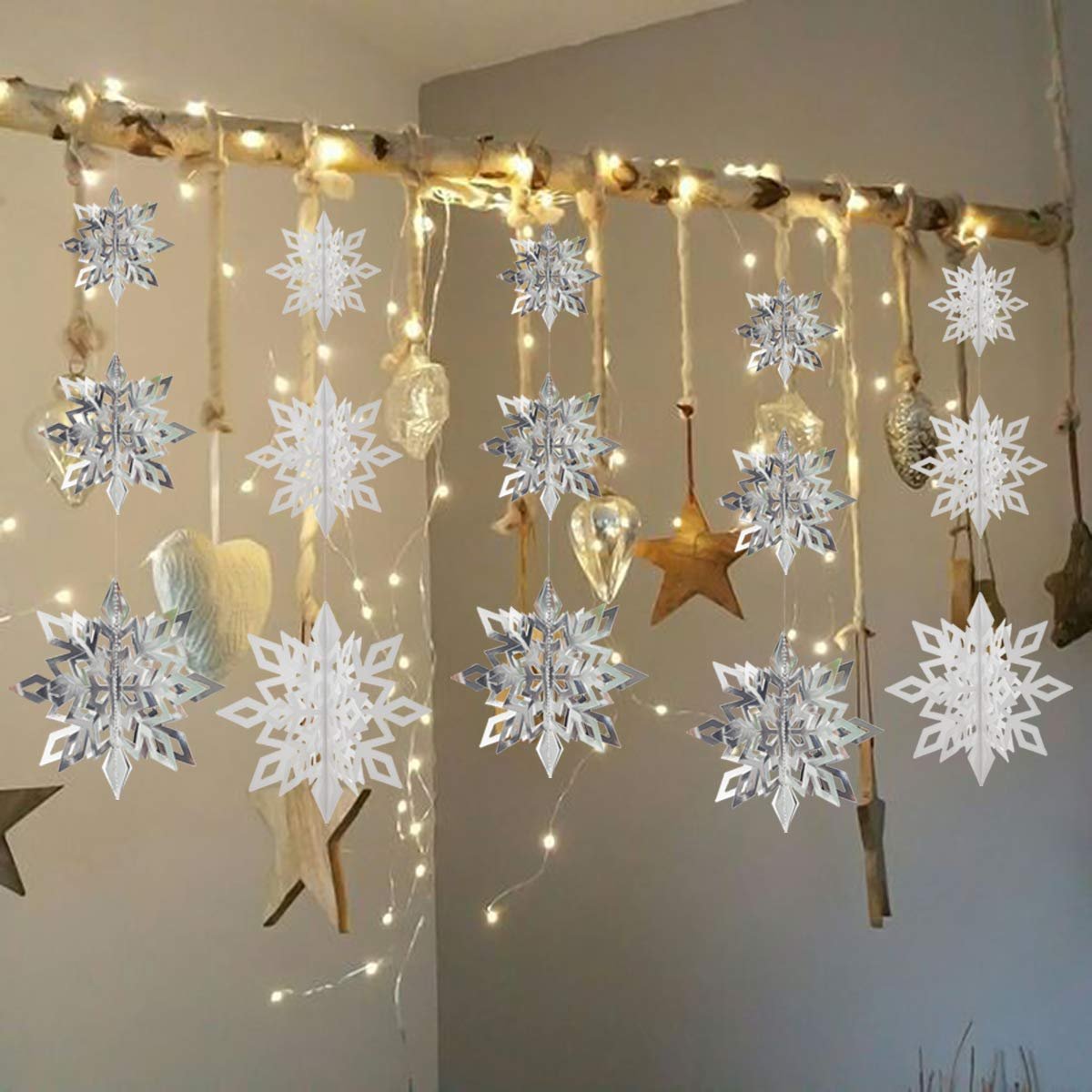 White and silver 3D paper snowflake ornaments hanging from a branch with fairy lights