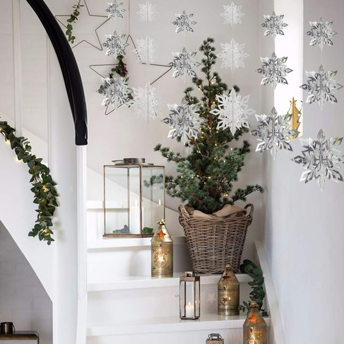Hanging 3D paper snowflakes and a small Christmas tree on a staircase with lanterns and garland