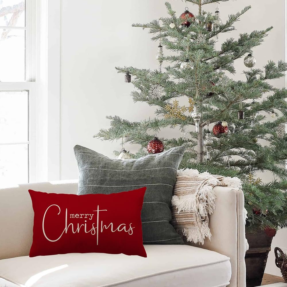 Red Christmas pillow cover with white 'merry Christmas' text on a couch next to a decorated tree