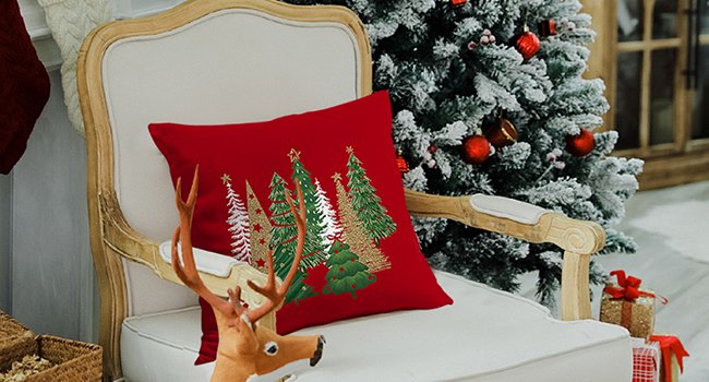 Red Christmas pillow with embroidered trees on a chair next to a decorated tree