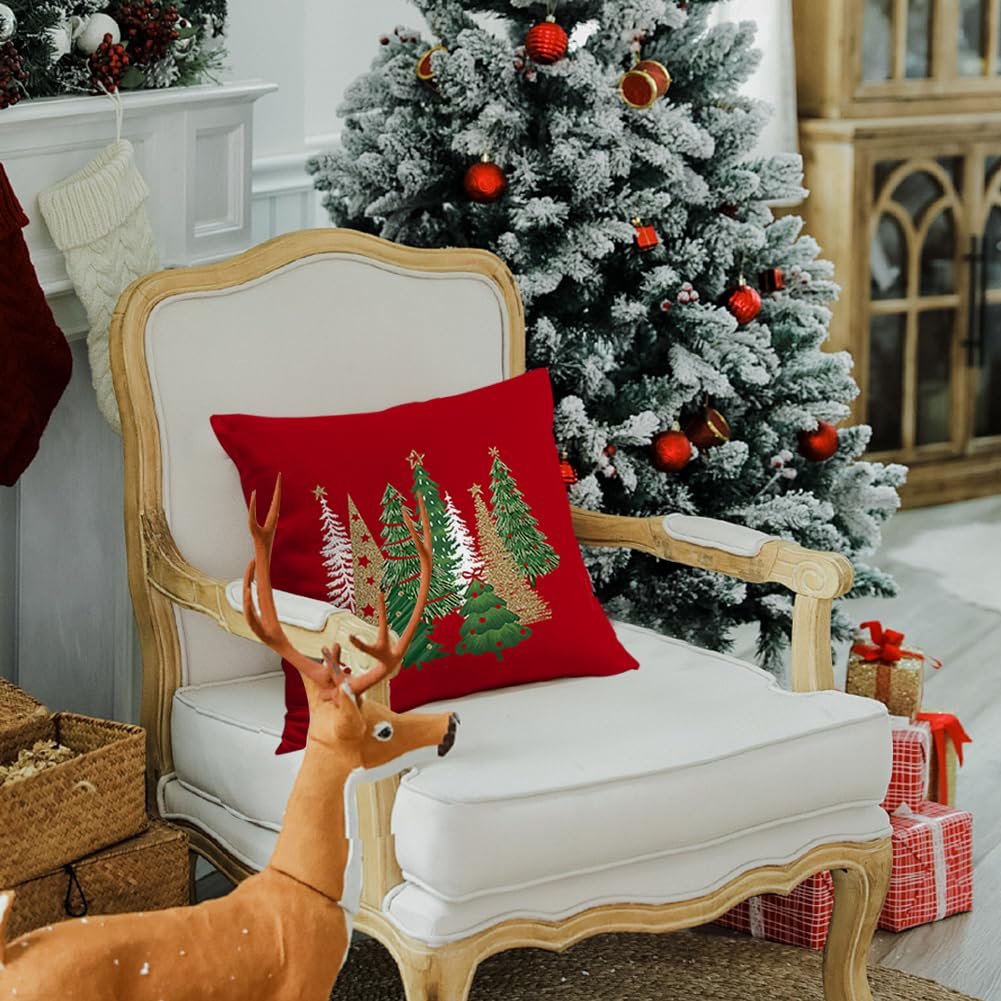 Red Christmas pillow with gold and green trees on a white armchair next to a decorated tree.