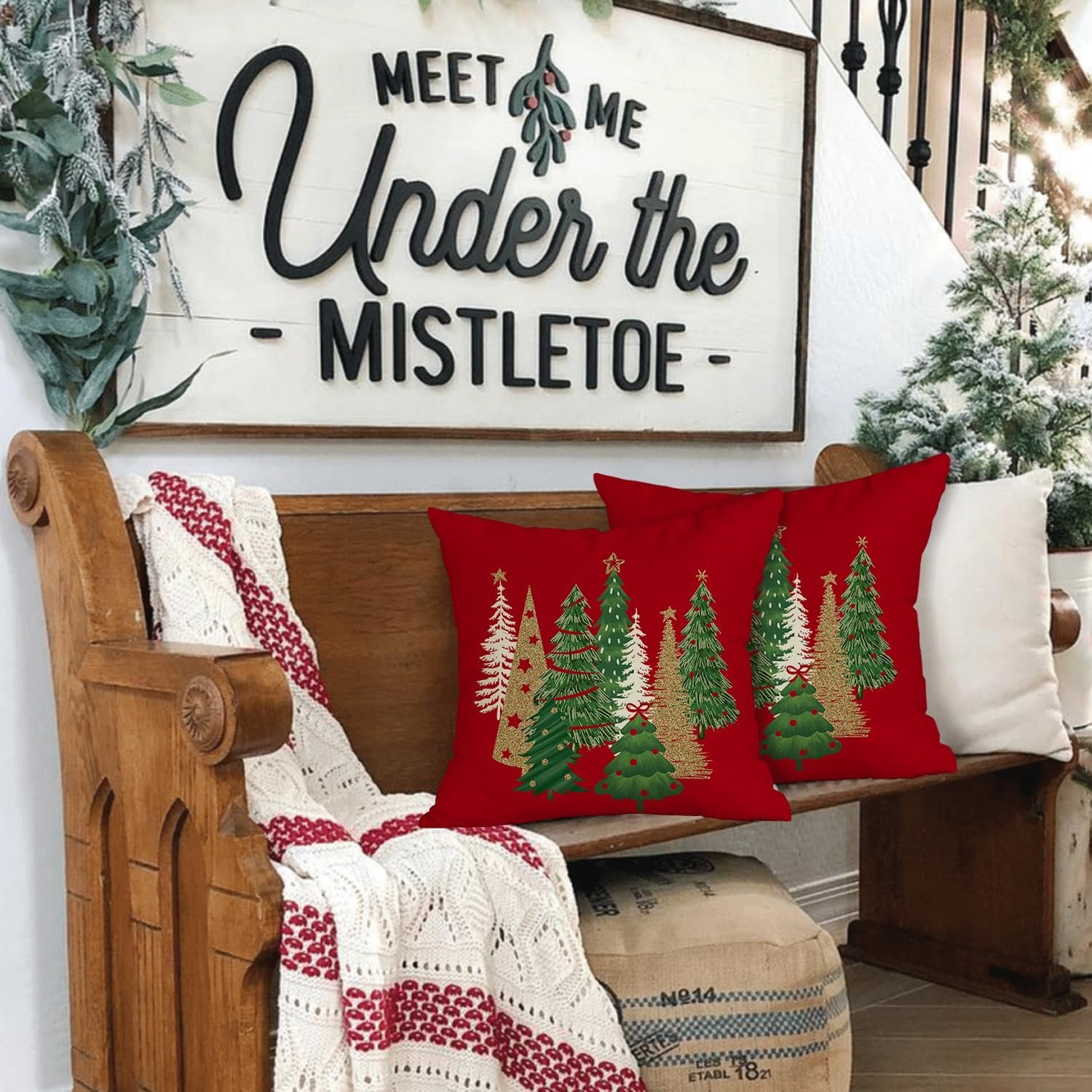 Two red Christmas pillow covers with green and gold trees displayed on a wooden bench with a blanket.