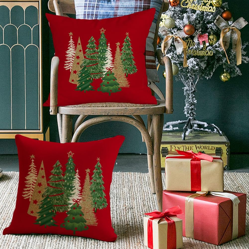 Two red Christmas pillow covers with green and gold trees displayed on a chair with gifts and a decorated tree in the background.