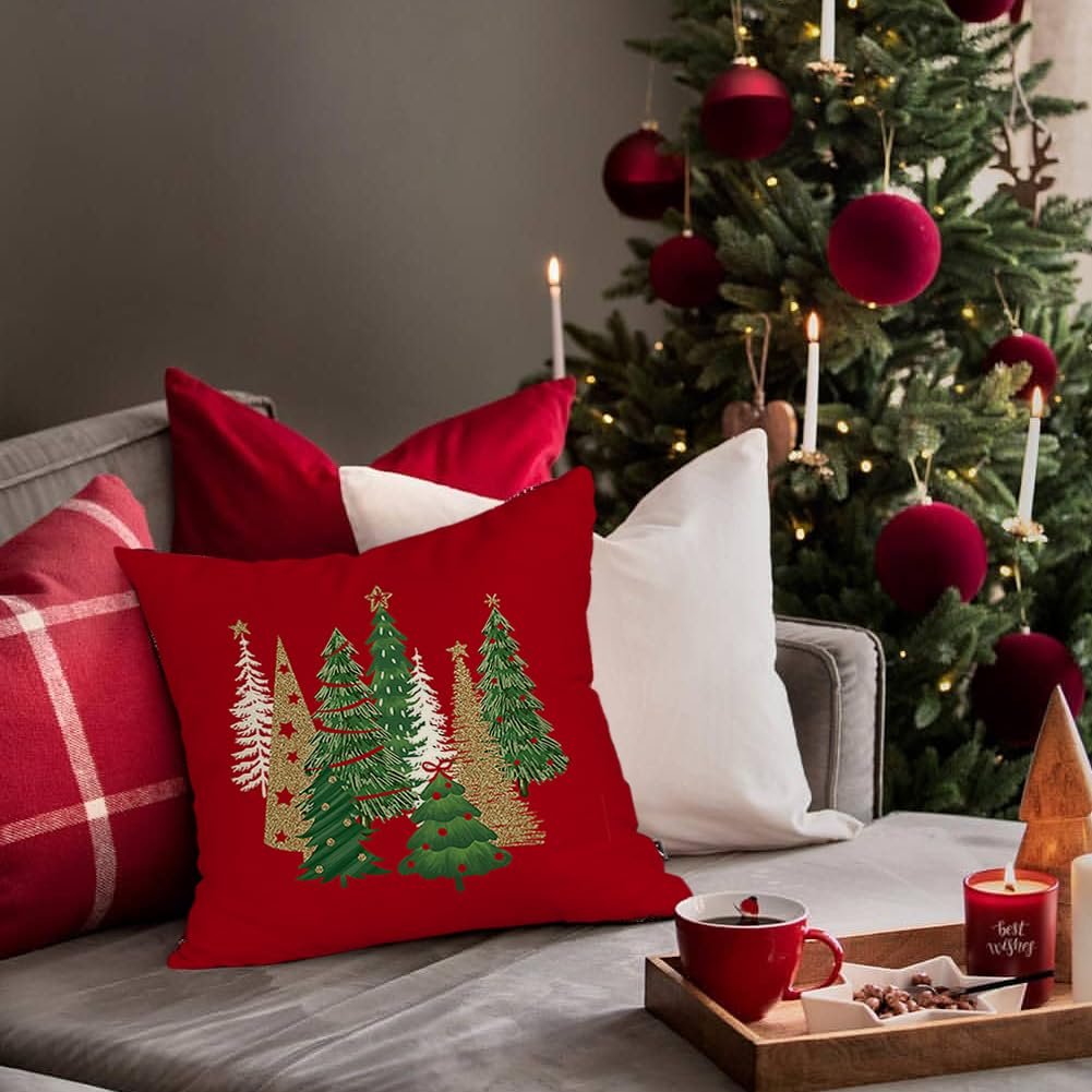 Red Christmas pillow cover with gold and green trees on a couch next to a decorated tree.