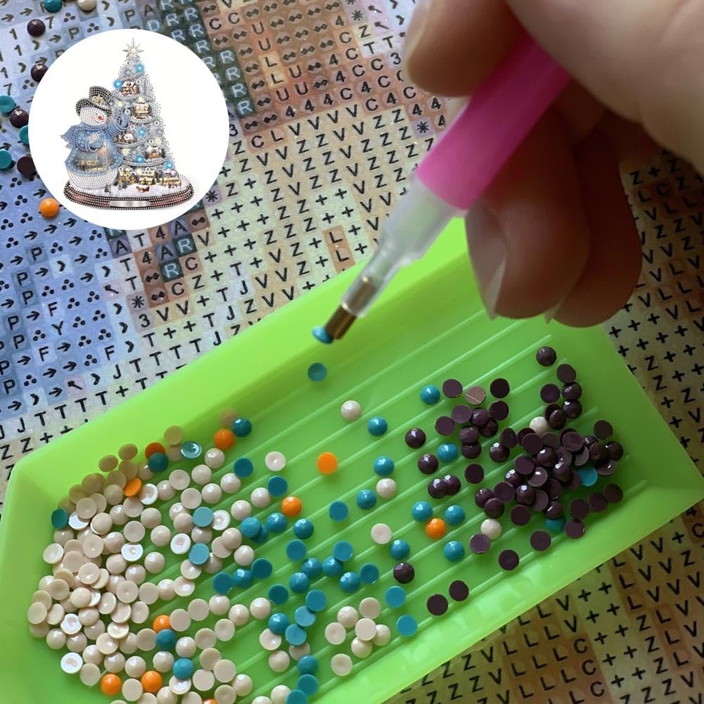 Diamond painting kit with a tray of colorful rhinestones and a pen being used to pick one up. A circular inset shows a finished diamond painting of a Christmas tree with snowmen.