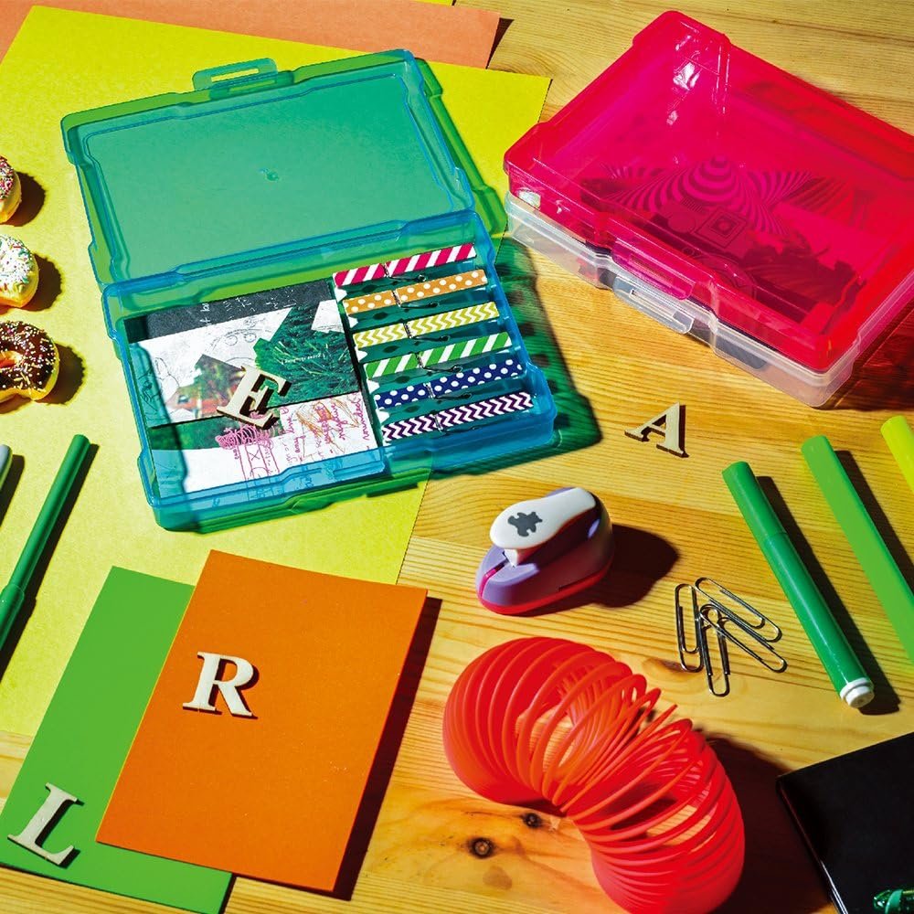Open green craft storage box with colorful washi tape and papers inside, next to a closed pink box and craft supplies on a wooden surface.