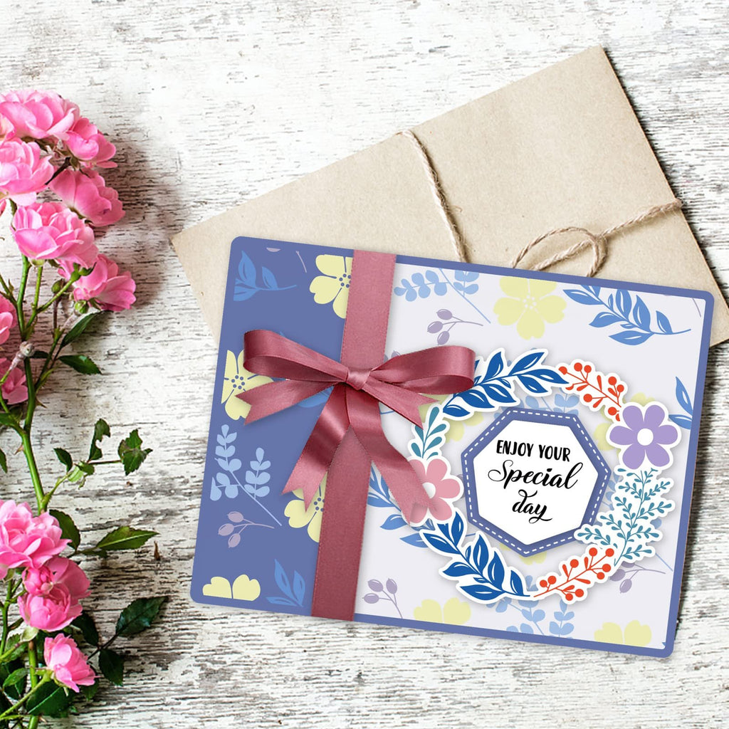 Card with floral design and ribbon, next to pink roses and an envelope.